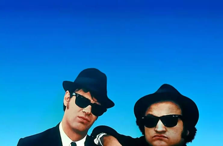 Two-men-in-black-with-glasses-and-hat-blue-screen