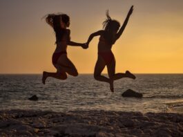 two-girls-jumping-on-the-beach-at-the-sunset