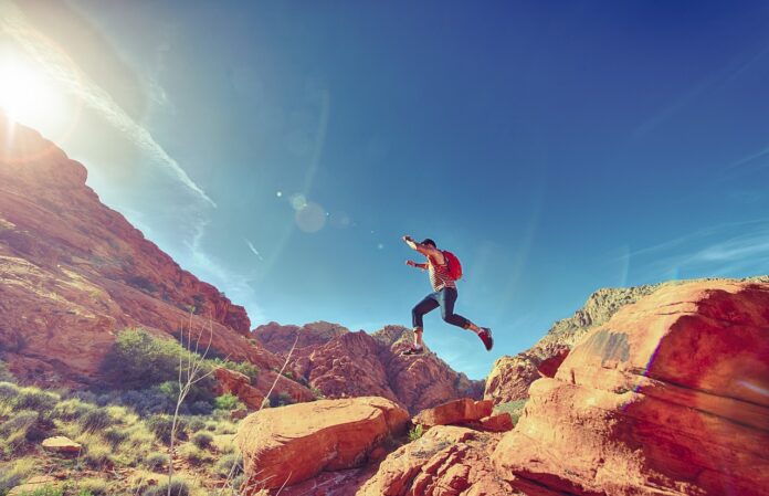 man-jumping-on-rocks-sky-blue-red-landscape