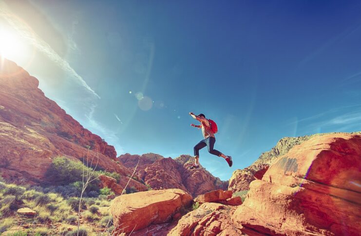 man-jumping-on-rocks-sky-blue-red-landscape